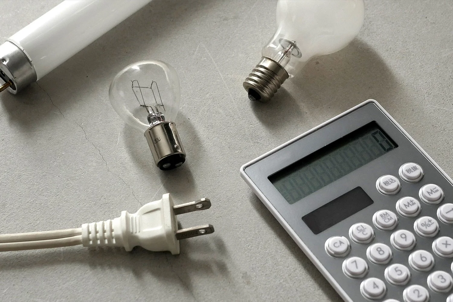 電球や電卓が写っており、電気代の計算や節電、エネルギー消費について考察する様子を連想させます。